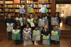 A group of people displaying their paintings together while smiling at the viewer.