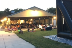 A large group of people sitting outdoors while watching a film on an inflatable projector.
